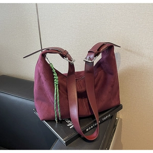 Detail of burgundy suede bucket bag with wide strap and green woven keychain charm