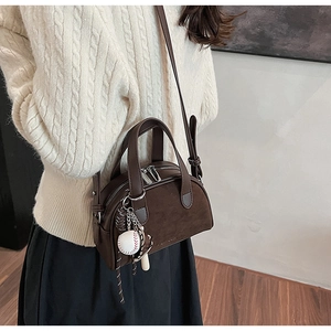 Detail van vintage bruine crossbody tas met honkbal hanger en getextureerd leer
