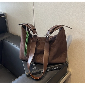 Detailed close-up of brown suede hobo bucket bag with adjustable leather strap and green charm