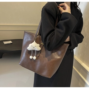 Brown leather tote bag worn on shoulder with a cute cloud plush pendant detail
