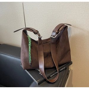 Detail of dark brown suede bucket bag with adjustable leather straps and green woven charm