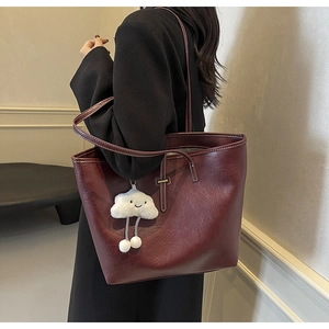 Deep red leather tote bag with cloud pendant shown on shoulder over black coat