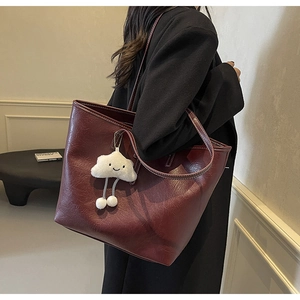 Detail view of large burgundy oil-wax leather tote bag with white plush cloud pendant