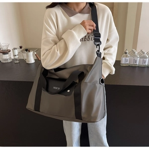 Dettaglio della grande borsa da viaggio NOCO indossata da una modella in un caffè moderno