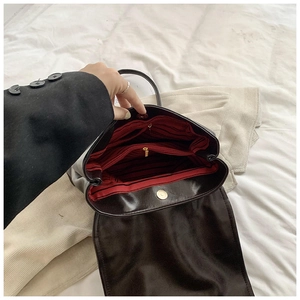 Close-up of black leather backpack interior with red striped lining and magnetic buckle