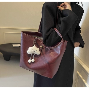 Detail of burgundy leather tote bag featuring a vintage texture and plush cloud charm