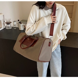Detailed side view of large khaki canvas travel bag with brown leather trim and red strap