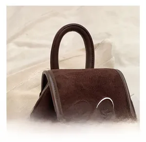 Detailaufnahme der braunen Veloursleder-Tasche mit verstärktem Griff und Silberschleife