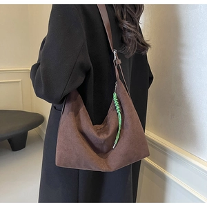 Detail of dark brown suede Hobo bag with green woven rope charm worn by model