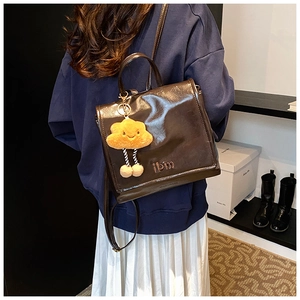 Detail of dark brown glossy backpack with metal logo and yellow cloud plush charm