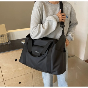 Detail van zwarte nylon reistas met verstelbare riem en NOCO-logo gedragen door een model