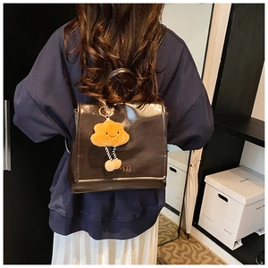Detail of dark brown glossy patent leather backpack with a cute yellow cloud plush charm