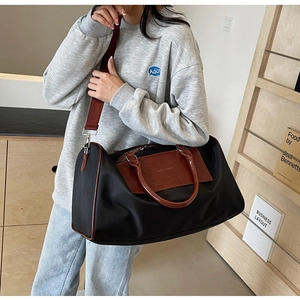 Black nylon travel bag with brown leather trim and red strap shown as a crossbody