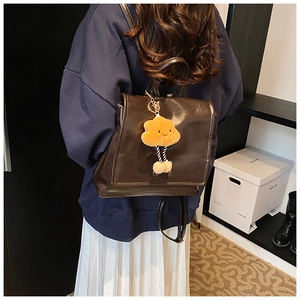 Detail of dark brown leather backpack with orange plush charm in a lifestyle setting