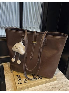 Brown leather tote bag with contrast stitching and cloud charm on art books