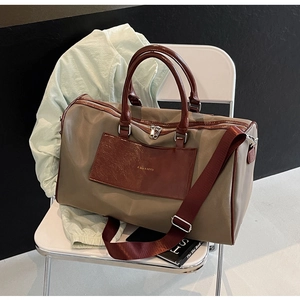 Detail of olive nylon travel bag with brown leather handles and a wide crimson strap