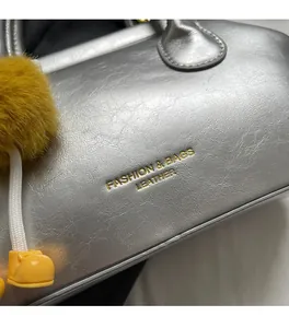 Dettaglio della borsa in pelle argento con scritte dorate e ciondolo pompon giallo