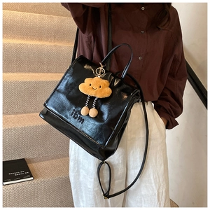 Detail of a shiny black leather backpack featuring a cute yellow cloud plush charm