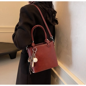 Deep red leather bucket bag with top handle and striped baseball charm detail