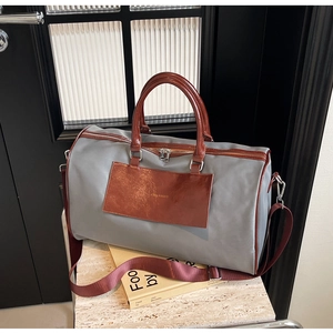 Detail of grey nylon travel bag with red-brown leather trim and dual zipper closure