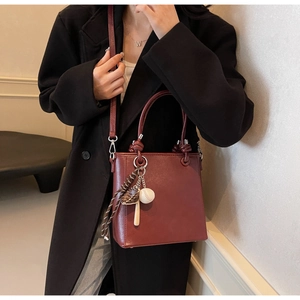 Close-up of burgundy lychee leather bucket bag with a baseball charm and crossbody strap