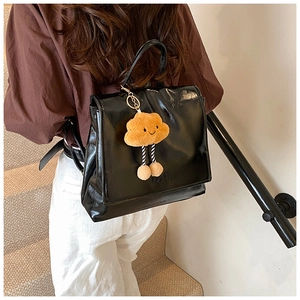Detail of a black glossy backpack featuring a cute orange cloud plush charm accessory