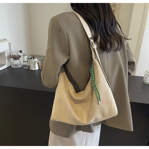Detail of a beige suede bucket bag with green braided rope knot shown on a model shoulder