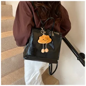 Detail of black glossy PU leather backpack featuring a cute brown cloud plush charm