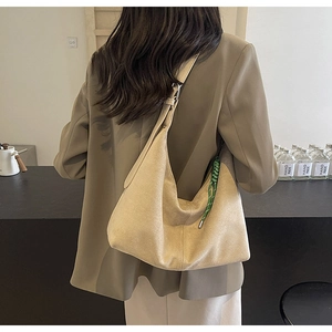 Detail of minimalist suede hobo bag with wide strap and green woven tassel charm