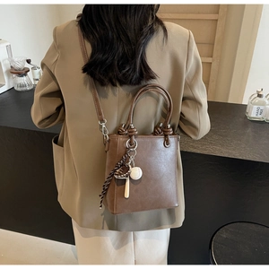 Detail of brown leather bucket bag with unique knotted handle and sports theme pendant