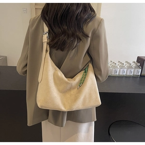 Détail d'un sac hobo en daim beige avec cordon tressé porté à l'épaule par un mannequin