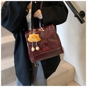 Detail view of burgundy glossy leather backpack with jbm embroidery and plush charm
