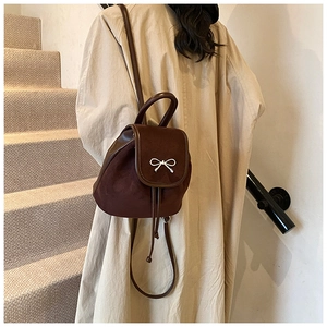 Detail eines dunkelbraunen Mini-Rucksacks mit Silberschleife auf beigem Trenchcoat