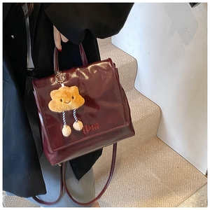 Detail of burgundy glossy leather backpack with red embroidery and plush cloud charm