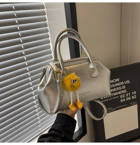 Dettaglio della borsa in pelle PU argento con ciondolo di peluche giallo e manici tondi