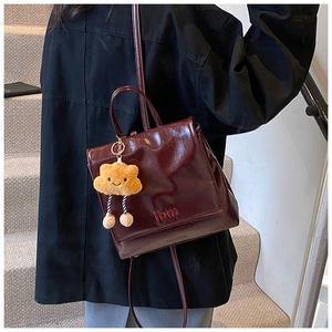 Detail of burgundy glossy leather backpack with ibm embroidery and yellow cloud pendant