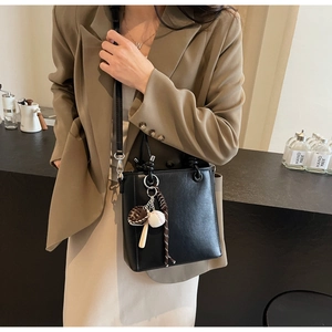 Close-up of black bucket bag featuring creative baseball-themed sports charms and silver hardware