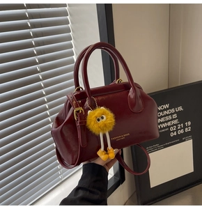 Dettaglio borsa in pelle verniciata bordeaux con logo dorato e ciondolo di peluche