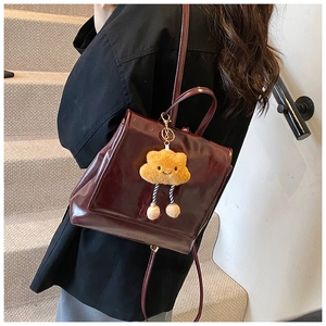 Detail of burgundy patent leather backpack with cloud plush charm on a model