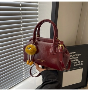 Dettaglio borsa in pelle bordeaux scuro con scritta dorata e ciondolo di peluche giallo