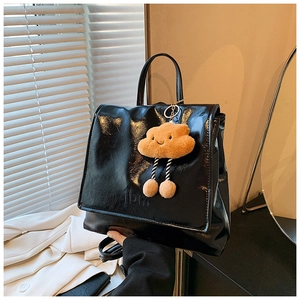 Detail of black glossy leather backpack with embossed letters and a cute plush charm