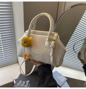 Dettaglio della borsa in pelle bianco crema con chiusura in metallo e ciondolo giallo