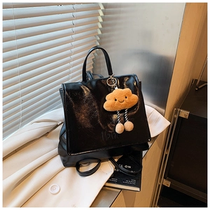 Macro detail of glossy black leather backpack with ilbm embossing and plush cloud charm
