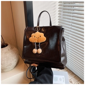 Detail of coffee brown glossy faux leather backpack with plush cloud charm and top handle