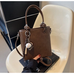 Detail of brown leather bucket bag with creative baseball pendant and tied handle