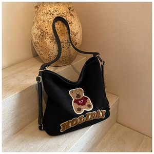 Detail of black canvas hobo bag featuring teddy bear embroidery and leather strap