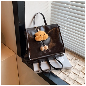 Detail of vintage brown leather backpack with a yellow plush cloud charm on a white book