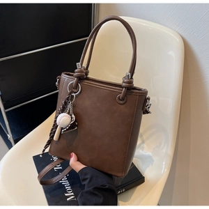 Detail of dark brown leather bucket bag with creative baseball glove bag charm