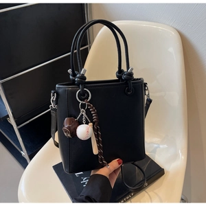 Detail of black leather bucket bag featuring a baseball-themed charm and knot handles