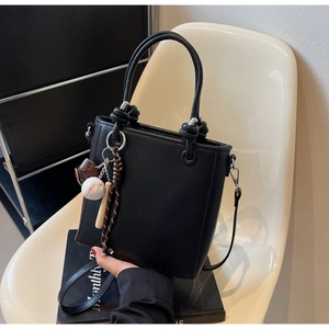 Detail of black bucket bag featuring baseball charms and adjustable shoulder strap